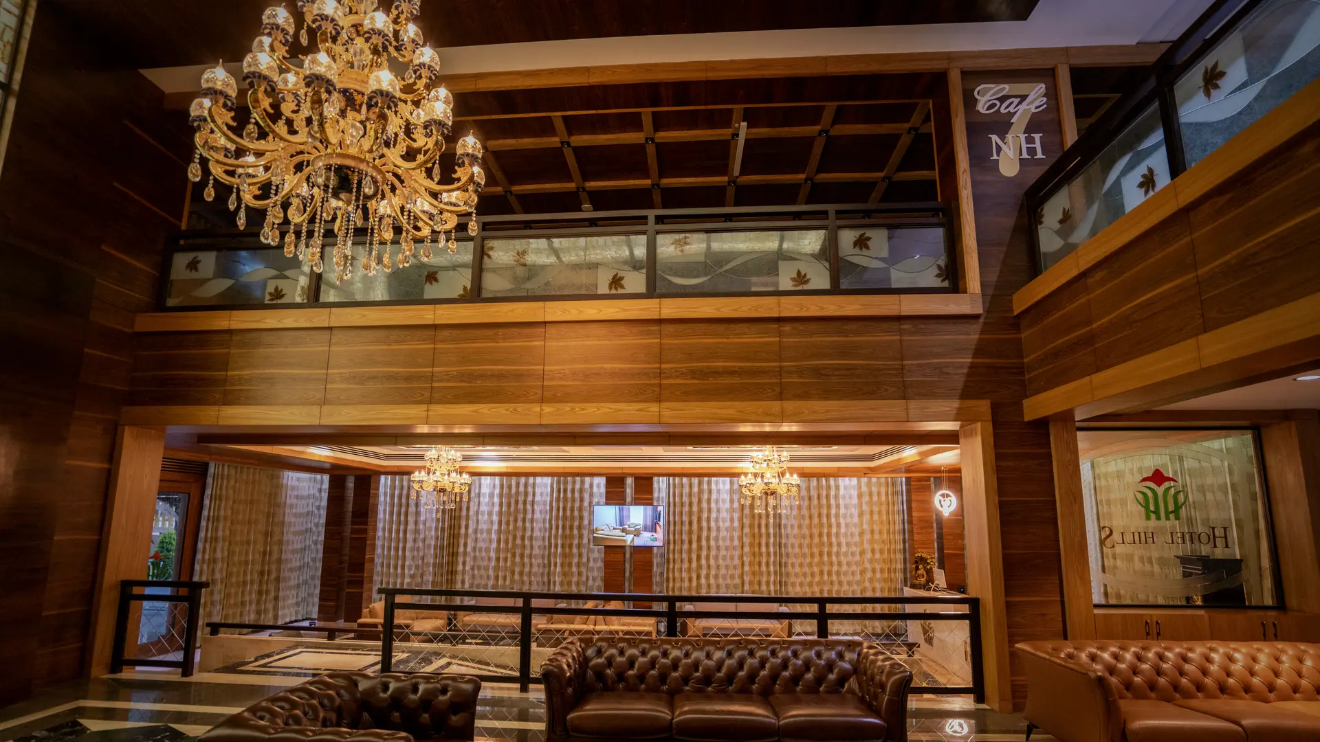 Leather Chesterfield sofas on the chequered marble floor of the lounge at Hotel Hills Hosur, a chandelier above and the cafe sign on the gallery