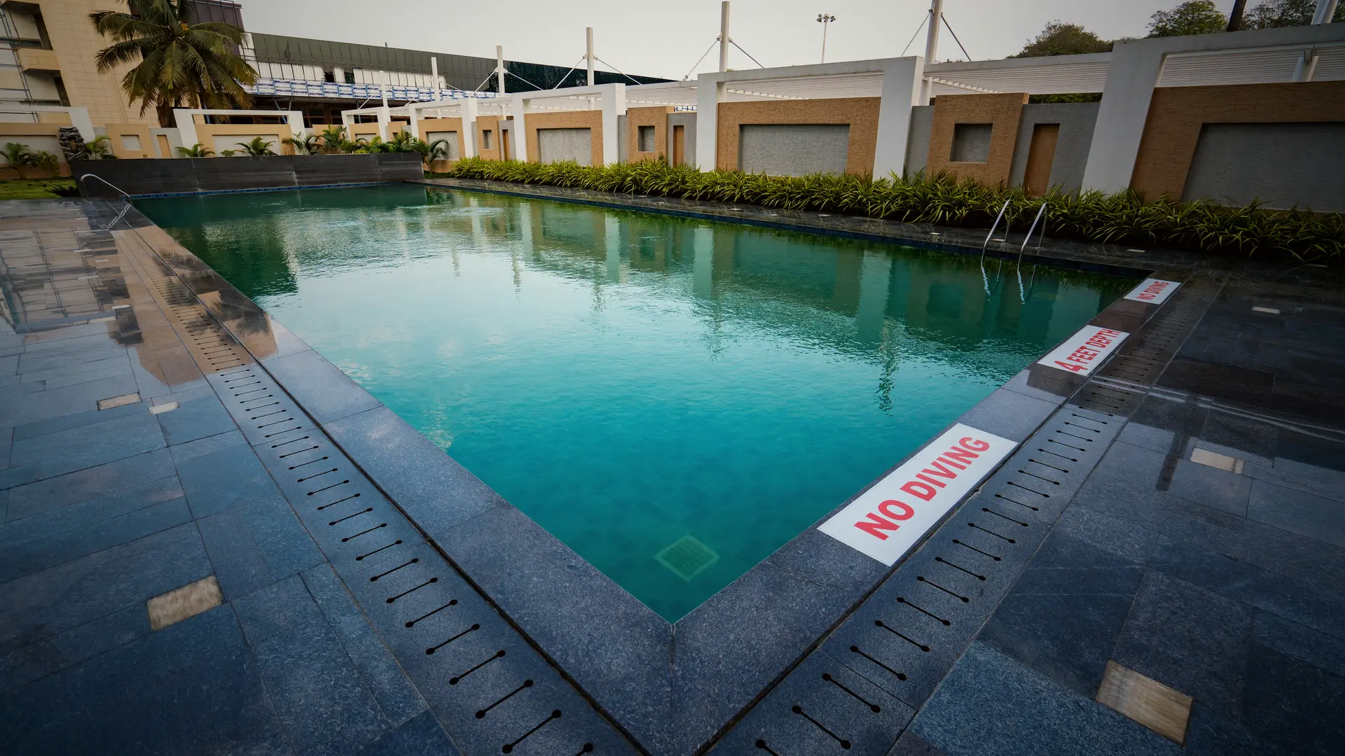 The pool at Hotel Hills Hosur from its far end, the granite deck running diagonally out of frame
