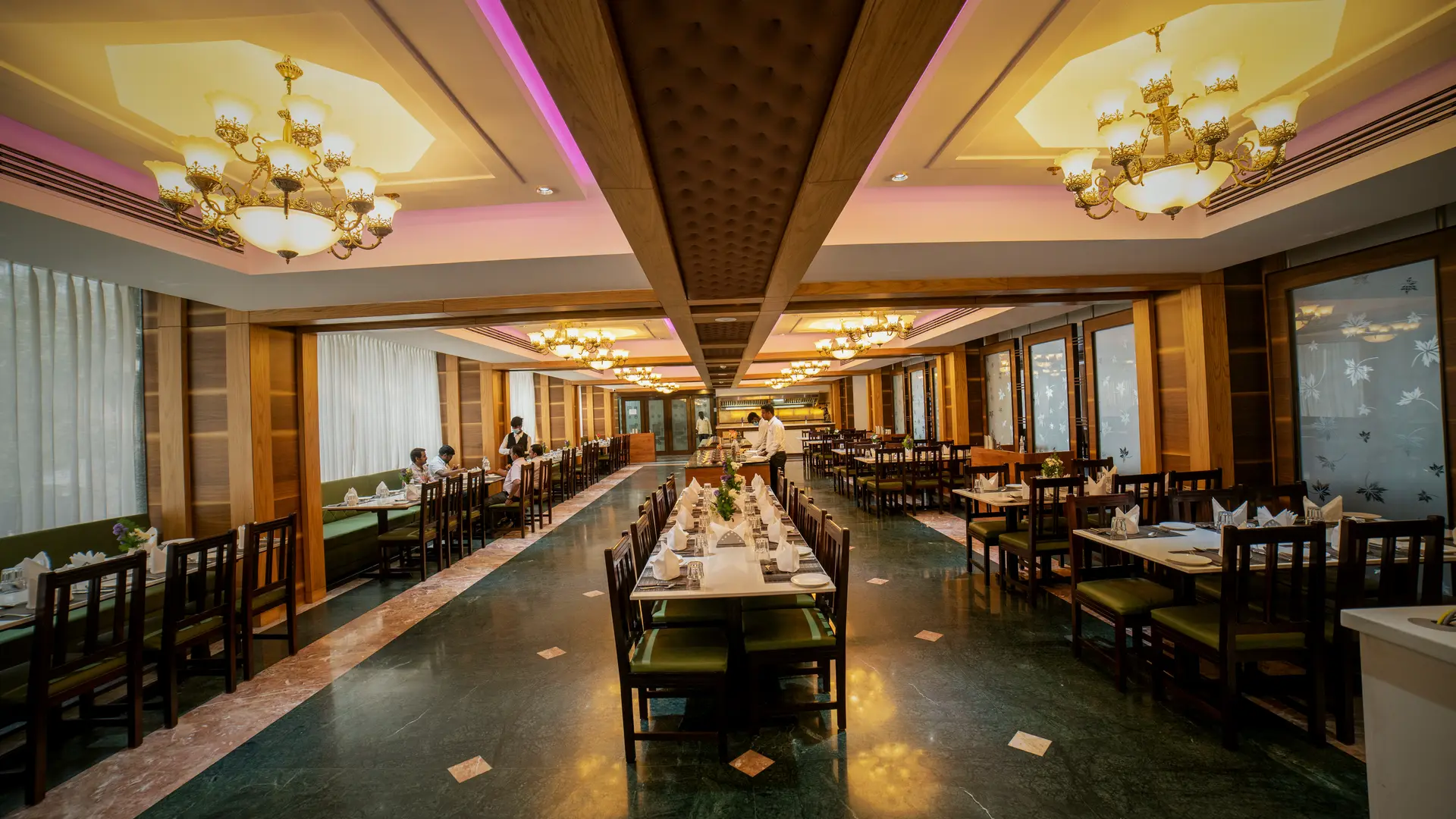 The Copper Bowl restaurant at Hotel Hills Hosur looking down the central aisle, tables laid either side, chandeliers in the coffered ceiling