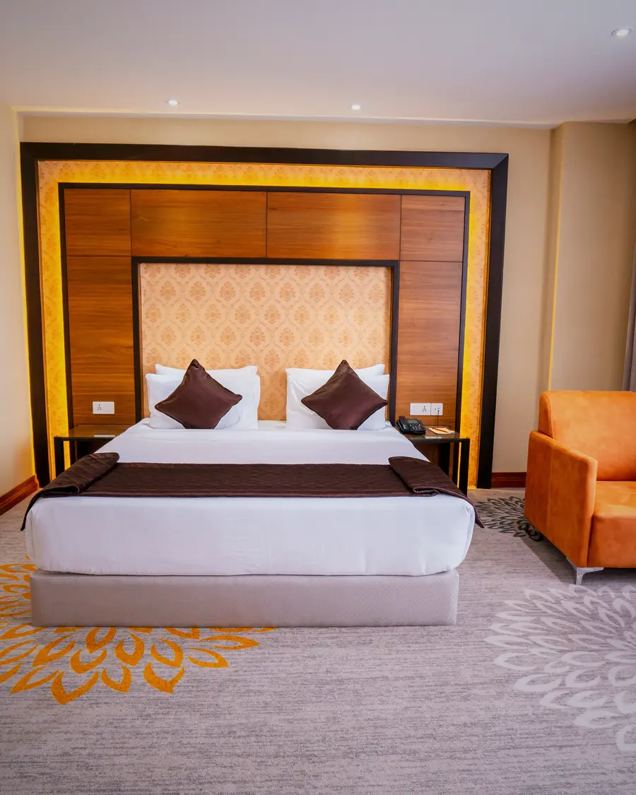 A king room at Hotel Hills Hosur, the bed against a lit timber headboard