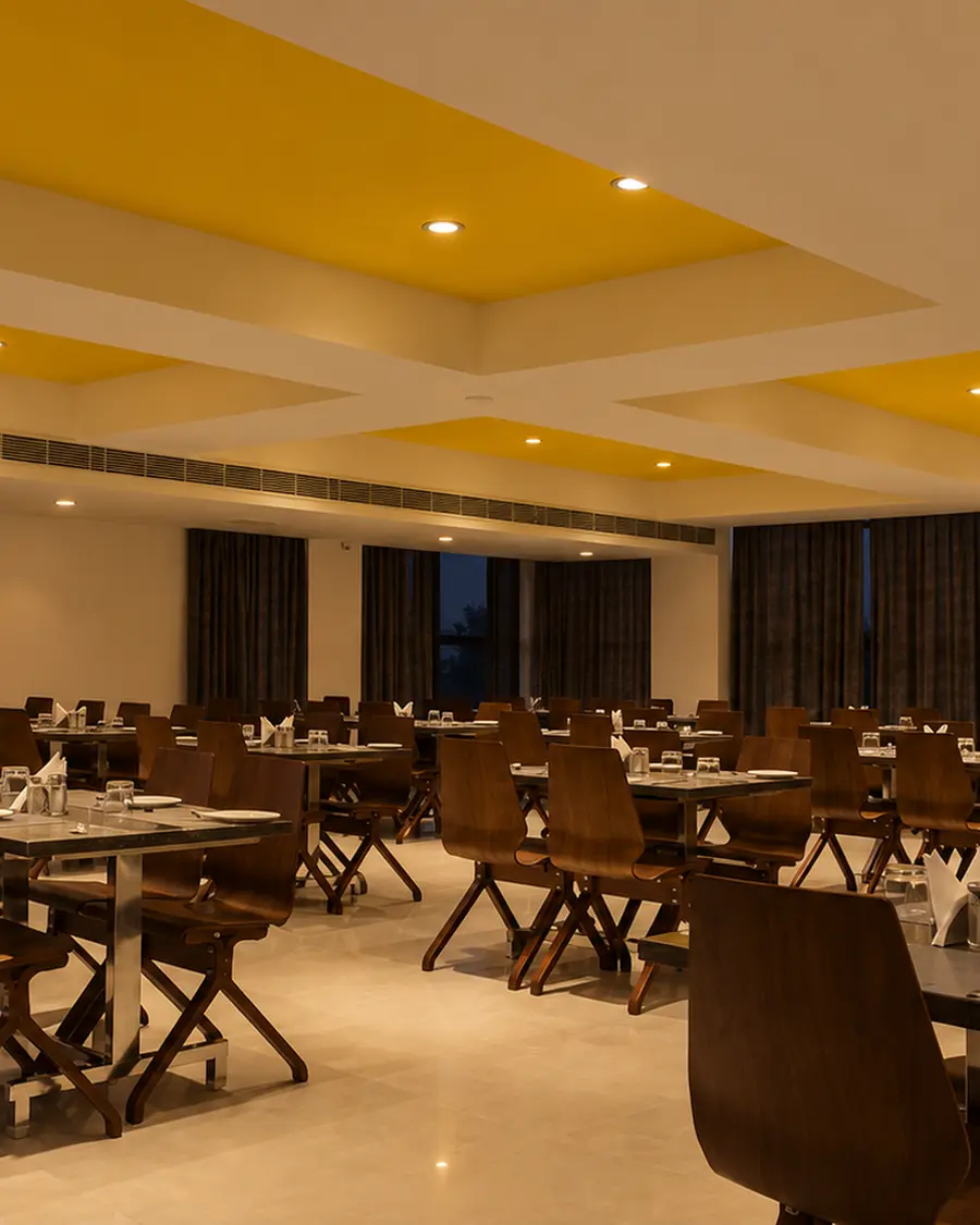 The restaurant at Hotel Hills Tirupattur, tables laid under a yellow ceiling panel